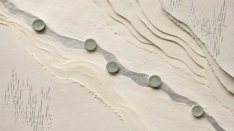 A silver river passes through ivory paper contours and five widely spaced celadon discs.